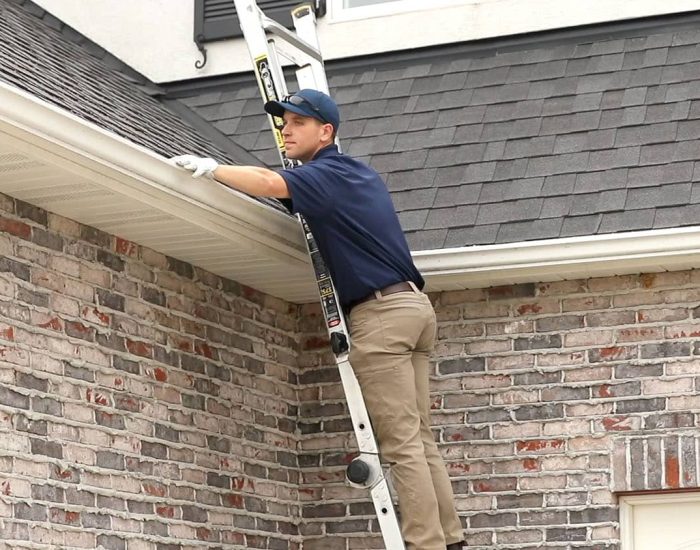 gutter cleaning professional on ladder cleaning gutter on brick home